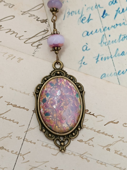 Collier pendentif vintage avec cabochon en verre Confetti rose et orange, monture laiton filigrane, sur fond de lettres anciennes.
