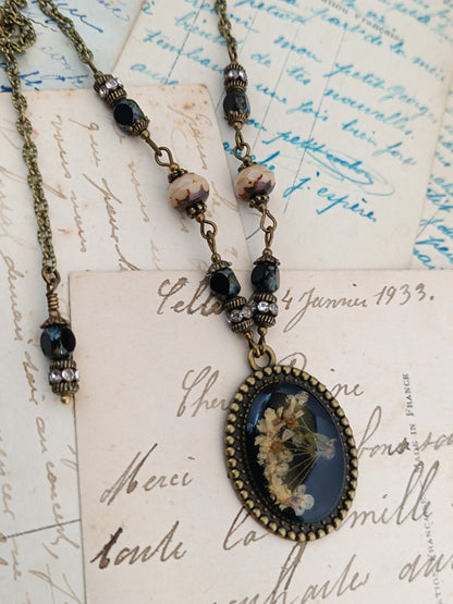 Collier cottagecore artisanal en résine et fleurs séchées sur fond noir, monture en bronze antique et perles de verre tchèque par Nathalie Aucoudesanges