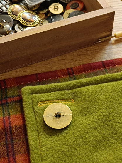 Bouton vintage doré vu de dos, posé sur tissu polaire vert pistache en cours de confection. Boutonnière réalisée en fil jaune, encore non ouverte. Détail d’atelier textile montrant le soin apporté aux finitions et à la préparation du montage.