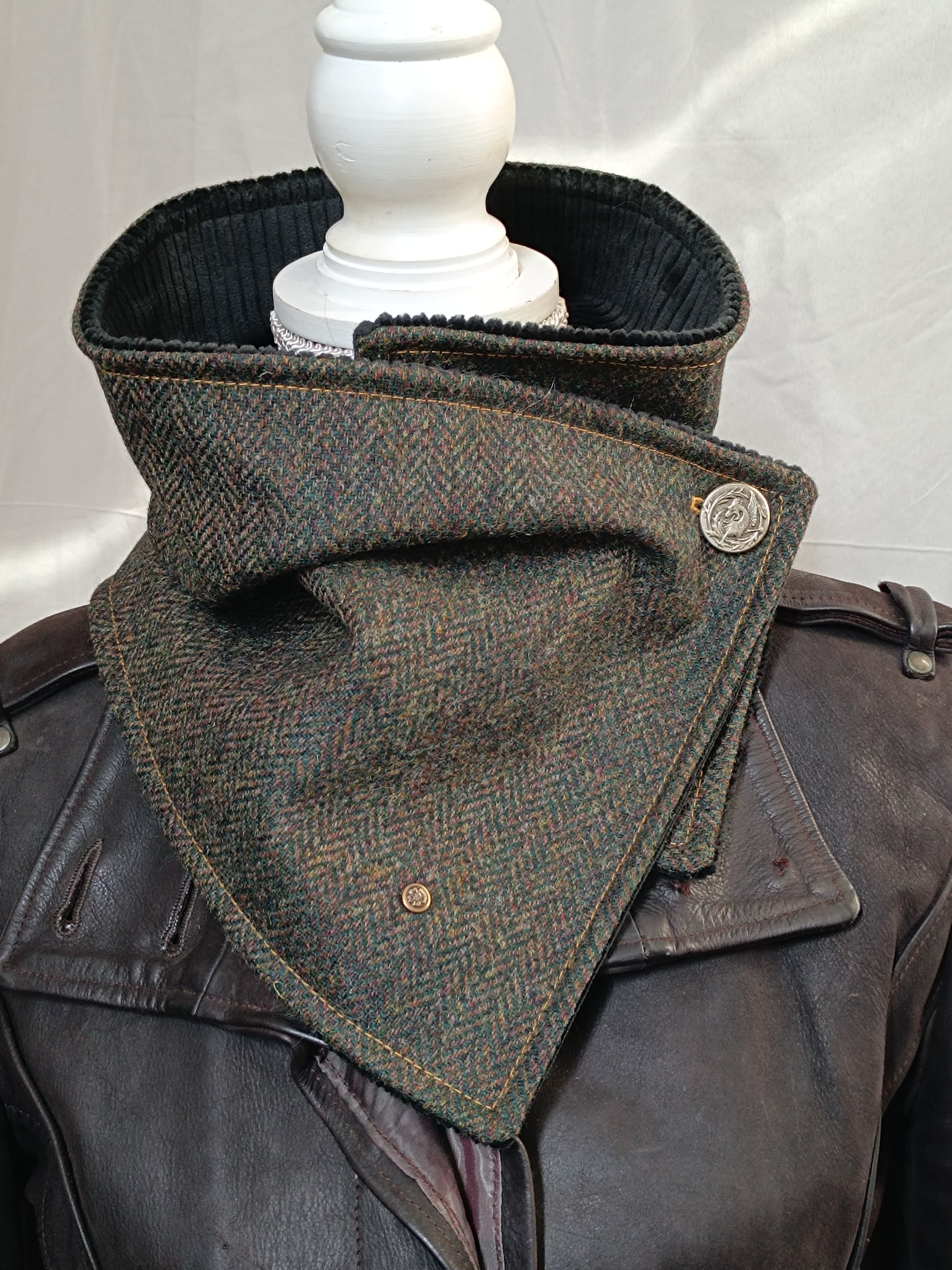 Écharpe boutonnée col de bénitier en laine à chevrons vert, brun et ocre, doublée velours côtelé noir. Ce tour de cou artisanal peut se draper en col montant structuré, se replier façon bénitier souple ou s’ouvrir légèrement pour dévoiler sa doublure texturée. Fermeture par boutons métal décoratifs, dont un dragon vintage. Création unique réalisée dans notre atelier de l’Oise.