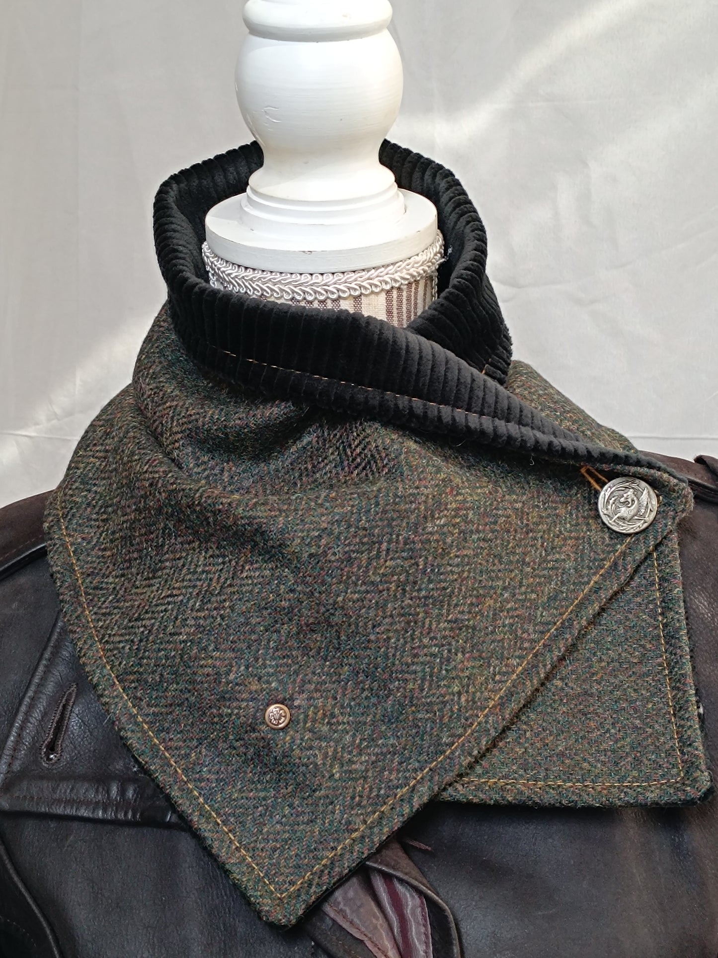 Écharpe boutonnée col de bénitier en laine à chevrons vert, brun et ocre, doublée velours côtelé noir. Photo prise en intérieur pour restituer fidèlement les couleurs sans lumière artificielle. Boutons métal décoratifs, dont un dragon vintage. Accessoire artisanal chaud et élégant, réalisé dans notre atelier de l’Oise.