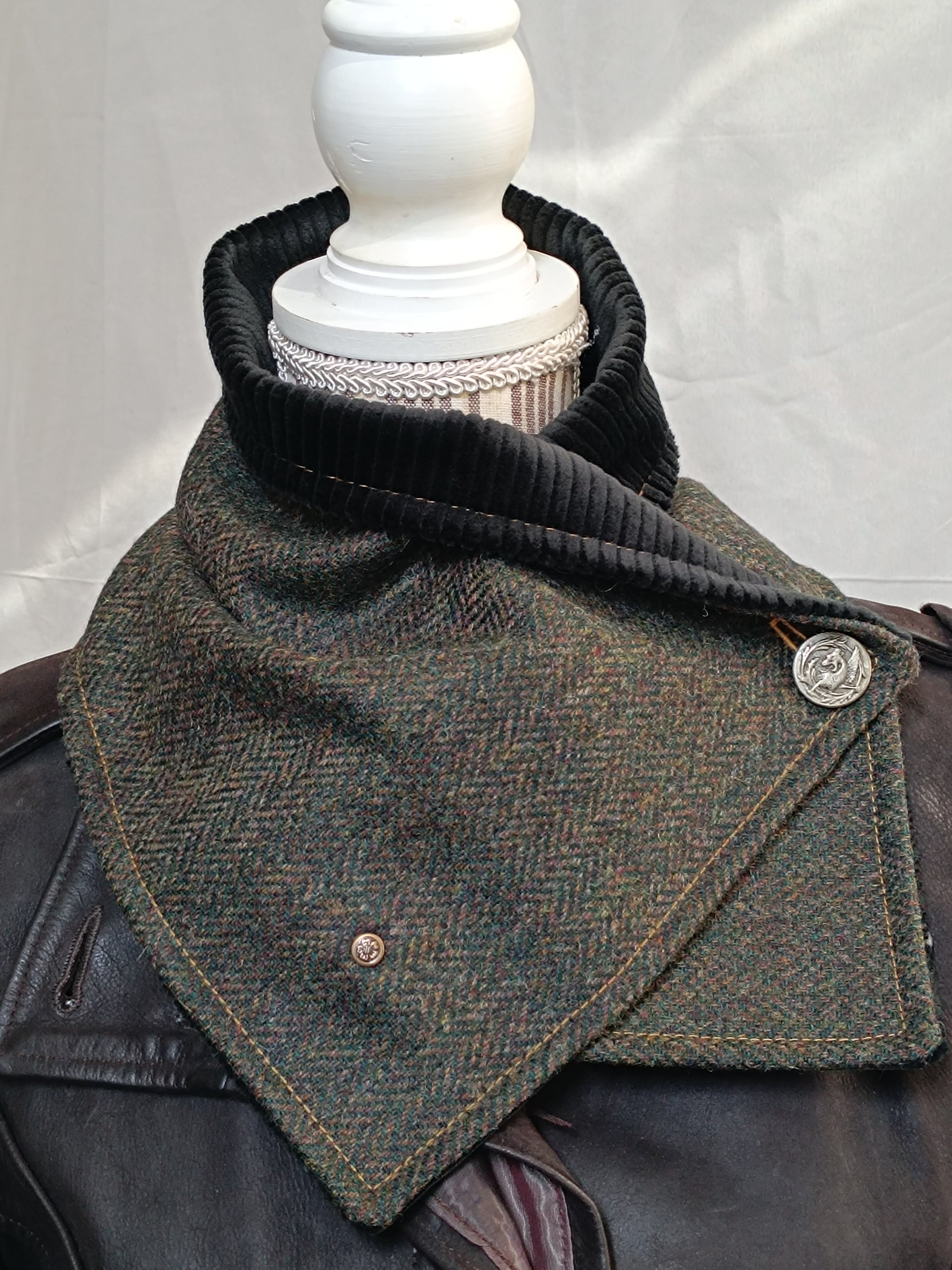 Écharpe boutonnée col de bénitier en laine à chevrons vert, brun et ocre, doublée velours côtelé noir. Photo prise en intérieur pour restituer fidèlement les couleurs sans lumière artificielle. Boutons métal décoratifs, dont un dragon vintage. Accessoire artisanal chaud et élégant, réalisé dans notre atelier de l’Oise.
