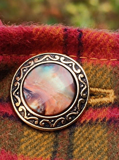 Bouton vintage doré à motif central coloré évoquant la nacre, monté sur tartan en lainage doux rouge, vert et jaune. Bordure en métal finement ciselée, détail emblématique du tour de cou artisanal.