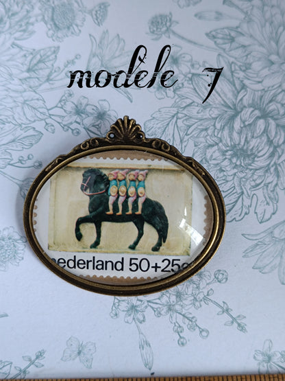 Broche ovale encadrant un timbre néerlandais vintage du siècle dernier, illustré d’un cheval noir portant cinq personnages stylisés, sur fond beige, avec la mention "Nederland 50+25c". Présentée sur un fond fleuri aux motifs botaniques bleu clair.