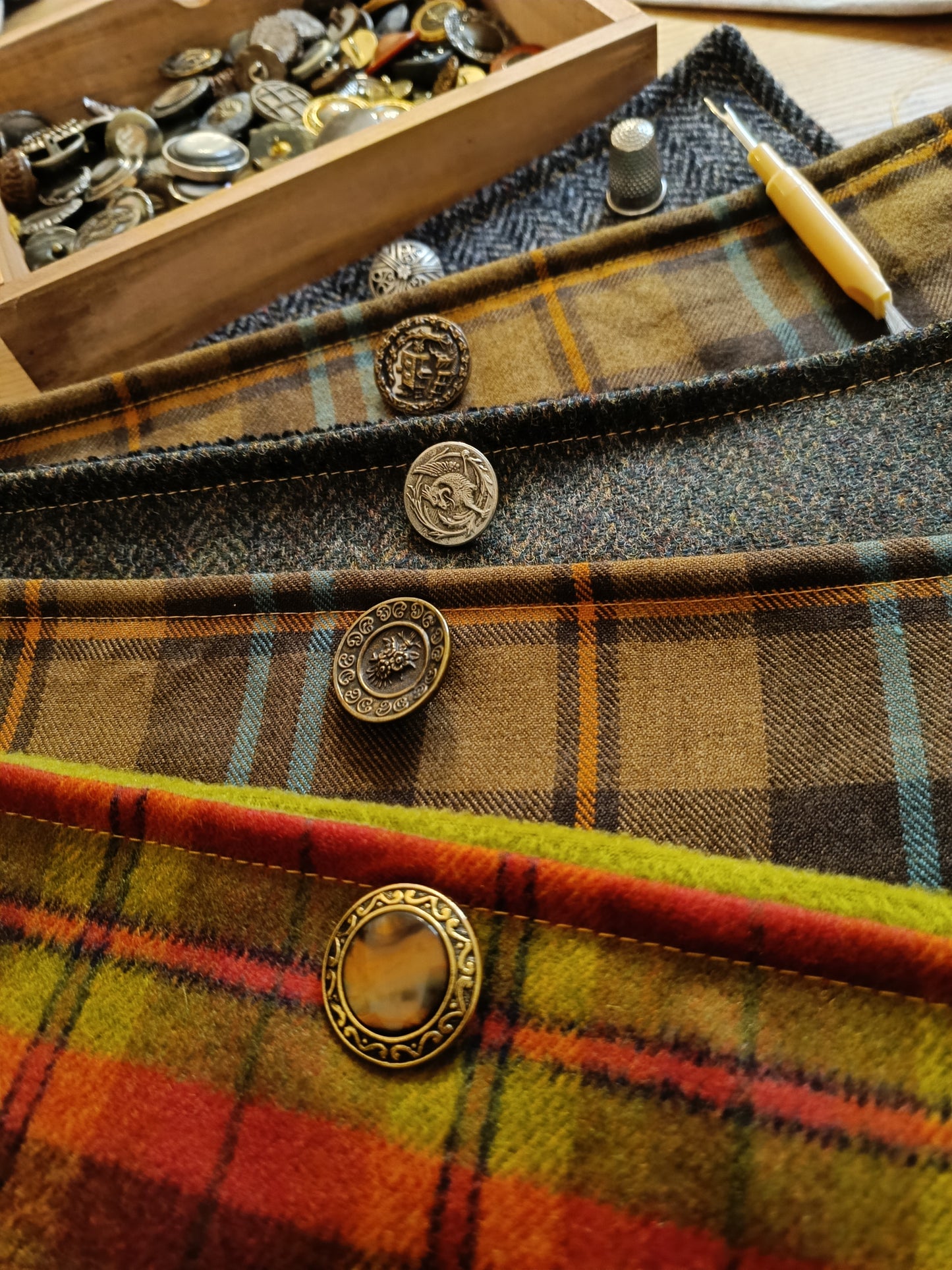 Échantillons de créations textiles réalisées par l’atelier : cols boutonnés et accessoires en laine grattée, tartan ou chevrons, chacun orné d’un bouton vintage unique. Palette de couleurs riche et finitions soignées. Présentation artisanale mettant en valeur le savoir-faire et les possibilités de personnalisation.