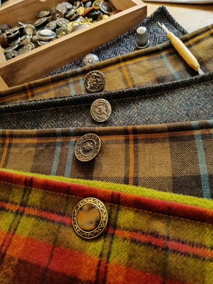 Échantillons de créations textiles réalisées par l’atelier : cols boutonnés et accessoires en laine grattée, tartan ou chevrons, chacun orné d’un bouton vintage unique. Palette de couleurs riche et finitions soignées. Présentation artisanale mettant en valeur le savoir-faire et les possibilités de personnalisation.