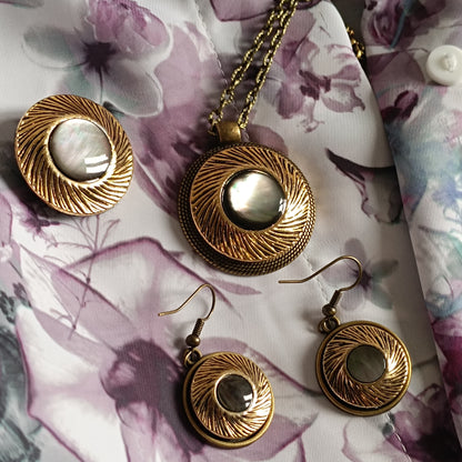Parure de bijoux vintage en bronze antique et nacre irisée posée sur tissu fleuri clair violet pour montrer l’effet du bijou sur vêtements féminins lumineux. Ensemble artisanal rétro comprenant collier, boucles d’oreilles et broche. Le charme vintage français 